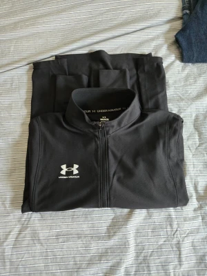 Svart träningsjacka Under Armour - Svart tröja från Under Armour med hel dragkedja och hög krage. 