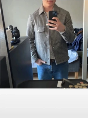 Grå overshirt med rutigt mönster - Snygg grå overshirt med diskret rutigt mönster och klassisk krage. Två bröstfickor med lock och knappar framtill. Perfekt lager-på-lager-plagg för en stilren look. Passar till jeans och t-shirt för en avslappnad vibe.