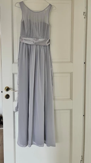 Ljusgrå balklänning med rosett i bak - Ljusgrå långklänning från Zalando som endast är använd en gång. Den har ett band i midjan av satin som går att knyta i bak. Klänningen passar någon som är  160 💗