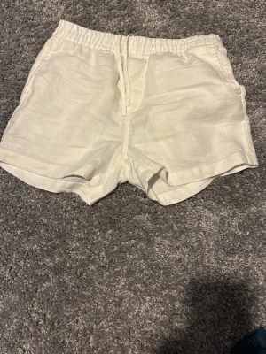 Vita linneshorts med snörning - Snygga vita shorts i linne med elastisk midja och snörning framtill. De har en avslappnad passform och fickor både fram och bak. Perfekta för varma sommardagar och ger en fräsch och stilren look.