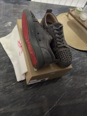 Christian Louboutin gråaa sneakers med spikar  - Grymma gråaa sneakers från Christian Louboutin med spikar och klassisk röd sula. Skorna har snörning och är gjorda i mocka för en lyxig känsla. Perfekta för dig som vill sticka ut med en edgy stil. Knappt använda/ köpte dem innan jag åkte på semester för 1 månad sen. 