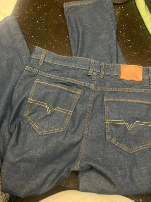 Blå raka jeans från Jeans Wear - Säljer ett par klassiska blå jeans från Jeans Wear med raka ben och kontrastsömmar. Jeansen har fem fickor, bälteshällor och snygga detaljer på bakfickorna. Perfekta för en avslappnad och stilren look.