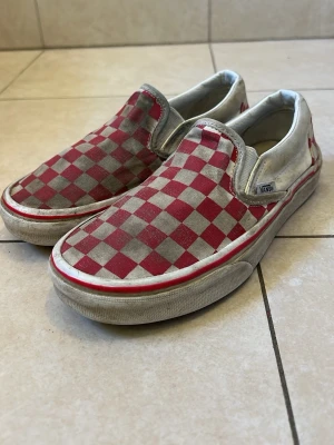 Vans slip-on rödvit checkerboard - det är en väldigt rare model från vans som är super sällsynt Klassiska Vans slip-on sneakers med röd och vit checkerboard-mönster. Skorna har låg profil, elastiska sidor och vit sula med röd rand. Ovandelen är i canvas och insidan är vadderad för extra komfort. Perfekta för en avslappnad streetstil.