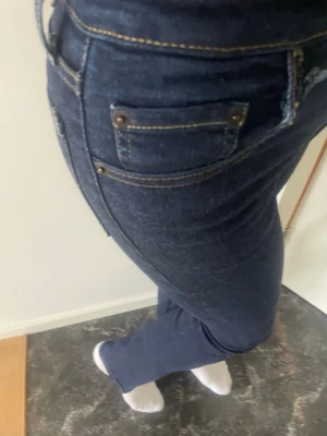 Mörkblå slim fit jeans - Snygga mörkblå slim fit jeans med klassiska fem fickor och kontrastsömmar. Jeansen har en smal passform och normal midja, perfekta för en trendig och stilren look. Materialet är stretchigt denim som ger bra komfort hela dagen.