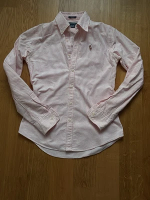 Rosa och vit randig skjorta från Ralph Lauren - Klassisk skjorta från Ralph Lauren i rosa och vitt med smala ränder. Knappt använd. Strl S. Pris kan diskuteras. 
