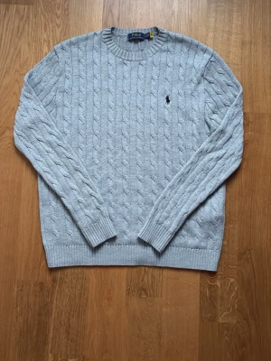 Grå stickad Ralph Lauren tröja  - Kabelstickad grå tröja från Polo Ralph Lauren med rund halsringning och broderad logga på bröstet. Perfekt nu till sommaren över en t-shirt. Matchar jätte bra med alla typer av jeans. Den är väl använd. Strl S. Pris kan diskuteras. 