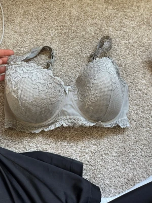 Grå spets-bh med vadderade kupor - Snygg grå bh med vadderade kupor och vacker spetsdetalj över hela framsidan och axelbanden. Bh:n har bygel, justerbara axelband och hakknäppning bak. Materialet är mjukt och stretchigt för extra komfort.