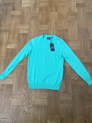Mintgrön stickad tröja Lyle & Scott - Fräsch mintgrön stickad tröja från Lyle & Scott i mjuk merinoull. Tröjan har rund halsringning, långa ärmar och ribbade muddar vid ärmslut och nederkant. Original pris 799kr