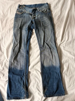 Diesel bootcut jeans med dip dye - Snygga blå bootcut jeans från Diesel med cool dip dye-effekt längst ner på benen. Klassisk femficksmodell med låg midja och detaljerade sömmar. Jeansen har en unik tvätt och är tillverkade i bomull med lite stretch för skön passform.