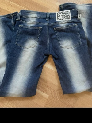 Blå bootcut jeans från Cheap Monday - Säljer ett par blå bootcut jeans från Cheap Monday med tydlig blekning längs benen och bakfickor. Jeansen har klassisk femficksdesign och en vit logopatch bak i midjan.💕
