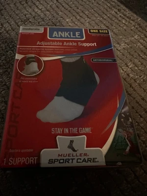 Mueller ankelstöd justerbart - Justerbart ankelstöd från Mueller Sport Care i svart, one size. Designat med patenterade remmar för extra stöd och komfort. Passar både höger och vänster fot och har antimikrobiell behandling. Perfekt för sport och träning där extra stöd behövs.