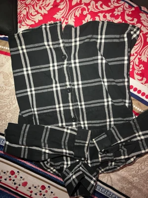 Svartvit rutig skjorta med knappar - Snygg svart skjorta med vitt rutmönster och knappar framtill. Skjortan har klassisk krage och raka ärmar. Perfekt för en trendig och avslappnad look.