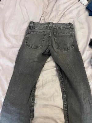 Grå bootcut jeans med två knapps knäppe - Snygga grå jeans med bootcut-modell och klassiska fem fickor. Jeansen har lätt slitna detaljer framtill och är tillverkade i denim med en skön stretch. Perfekta för en avslappnad och trendig look. Nackdelar, en liten fläck som förmodligen går att tvätta bort.
