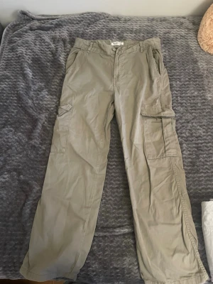 Pull&bear Gröna cargobyxor  - Säljer ett par  cargobyxor från pull&bear med raka ben och flera praktiska fickor på sidorna. Byxorna har klassisk cargostil med knapp och dragkedja framtill samt bälteshällor. Perfekta för en avslappnad och trendig look.