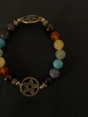 Färgglatt kristall armband med pentagram stjärna  - Unikt armband med pärlor med flera olika sorters kristaller. Armbandet har två detaljer i metall med pentagramsymboler som ger en mystisk vibe. Perfekt för dig som gillar alternativ stil och vill sticka ut med dina accessoarer. Köppt på en lokal kristall shop.