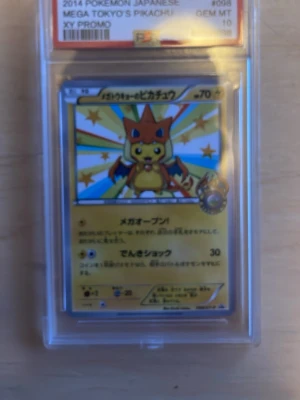 Mega Tokyo's Pikachu PSA 10 Pokémonkort - Obs ej orginal. Japanskt Pokémonkort med Pikachu utklädd till Mega Charizard, från 2014 och graderat PSA 10 GEM MT. Kortet är en XY Promo och har färger som gult, rött och blått. Kortet är inneslutet i ett genomskinligt plastfodral.