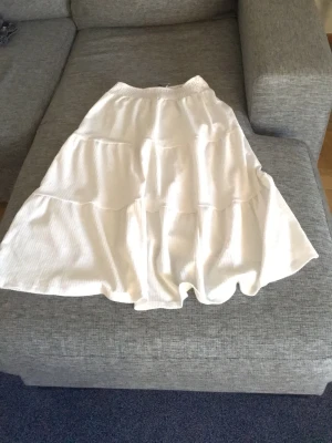 Vit volangkjol med resårmidja - Säljer en vit långkjol med flera volanger och resår i midjan. Kjolen har en luftig och flowy känsla, perfekt för varma dagar. Materialet känns mjukt och lätt, vilket gör den superbekväm att bära.💕