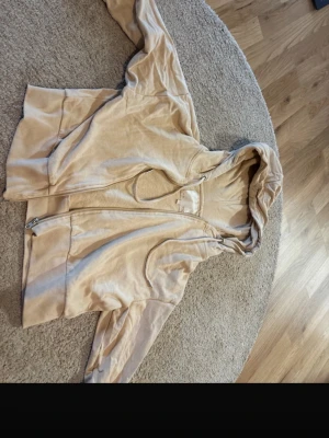 Beige velourhoodie från 157 - Mjuk beige hoodie i velour från 157 med dragkedja framtill och huva med dragsko. Hoodien har fickor på sidorna och en avslappnad passform. Perfekt för en chill och bekväm stil.