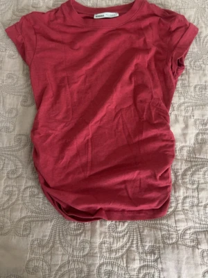 Röd t-shirt med snörning i sidan - Snygg röd t-shirt från Bershka i mjuk bomull. Modellen har korta ärmar och en cool snörningsdetalj i sidan som ger en unik twist. Perfekt till jeans eller kjol för en avslappnad men trendig look.