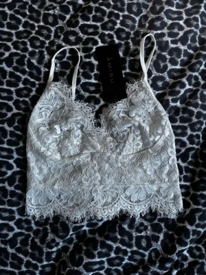 Vitt spetslinne från Amisu - Supersnygg vit linne från Amisu med tunna axelband och vacker blommig spets. Linnet har en feminin v-ringning, dekorativ kant och dragkedja bak. Perfekt för dig som gillar romantisk och trendig stil.