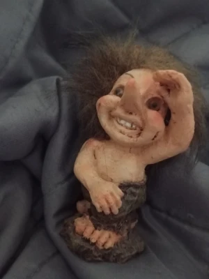 Liten trollfigur med lurvigt hår - Säljer en liten trollfigur med långt, brunt och rufsigt hår. Figuren har stora fötter och händer, samt bär en mörkbrun kjol. Tillverkad i ett hårt material, troligen resin eller keramik. Perfekt som dekoration eller samlarobjekt.