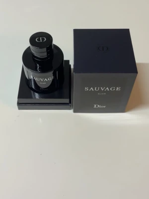 Dior Sauvage Elixir parfym - Dior Sauvage Elixir är en exklusiv parfym i en elegant, mörkblå glasflaska med silverfärgad text och rund form. Flaskan har en stilren svart kork med Dior-loggan på toppen. Kommer i matchande mörkblå kartong med tydlig märkning.