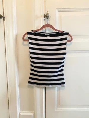 Randig ärmlös linnetopp - Säljer en svartvit randig linnetopp med breda horisontella ränder. Toppen är ärmlös och har en enkel, rak passform som sitter snyggt på kroppen. Perfekt för dig som gillar en clean och klassisk look.