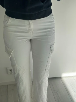 Vita cargobyxor med fickor - Säljer ett par vita cargobyxor med raka ben och stora sidofickor. Byxorna har klassisk cargostil med fickor både fram och bak samt på benen. Materialet känns mjukt och bekvämt, perfekt för en avslappnad look.