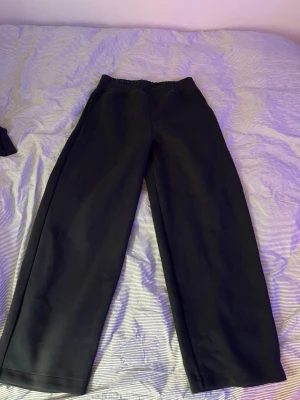 Svarta vida mjukisbyxor - Säljer ett par svarta mjukisbyxor med bred passform och resår i midjan. Byxorna har raka ben och två bakfickor. Perfekta för chill dagar hemma eller när du vill ha det extra bekvämt. Materialet känns mjukt och skönt mot huden.