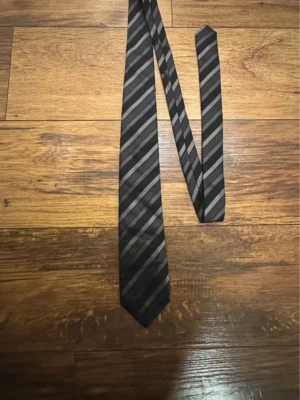 Svart slips med gråa ränder - Snygg svart slips med diagonala gråa ränder i olika nyanser. Använt 1 gång tror jag och den är i perfekt skick (säljer även på vinted)