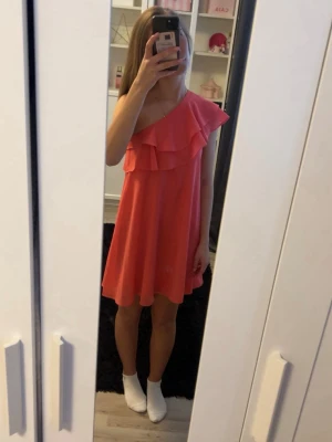 Rosa oneshoulder klänning med volang - Säljer en söt rosa kortklänning med oneshoulder och volangdetalj upptill. Klänningen har en luftig passform och är perfekt för varma dagar. Enkel och stilren design som ger en trendig look.