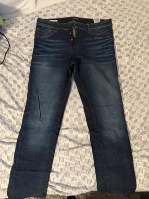 Slimstraight Mörkblåa raka jeans med knappar - Säljer ett par klassiska mörkblåa jeans med raka ben och snygga slitningar vid låren. Jeansen har knappgylf och kontrastsömmar som ger en cool look. Perfekta till vardagsoutfiten och passar till det mesta. Materialet är denim i bomull.