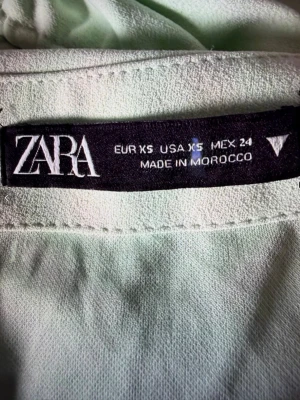 Ljusgrön kortkjol från Zara XS - Säljer en ljusgrön kortkjol från Zara i storlek XS. Kjolen har en tight passform med snygg snörning och rynkade detaljer längs sidan. Bluxtlås bak. Har innerkjol, men den är inte nerdragen på bilden. 