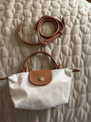 Beige axelväska  - Snygg beige axelväska med bruna läderdetaljer och guldfärgade metalldelar. Väskan har både handtag och avtagbar axelrem, samt klassisk knappstängning framtill. Perfekt för dig som gillar stilrena accessoarer.