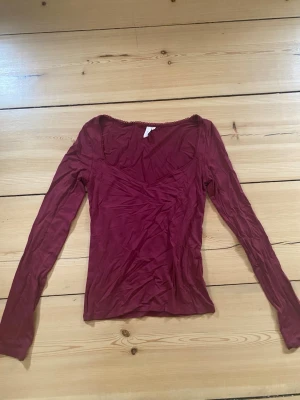 Vinröd långärmad topp med en urringning  - Snygg vinröd långärmad topp från Nelly och spetsdetalj längs halsringningen. Perfekt att styla med jeans eller kjol. Nästan helt oanvänd 