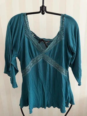 Turkos blus med spetsdetaljer storlek M-L - Snygg turkos blus med trekvartsärm och dekorativa spetsdetaljer längs ringningen och framtill. Blusen har en lös passform och är perfekt för dig som gillar en avslappnad men ändå feminin stil.Liten L mer som en M