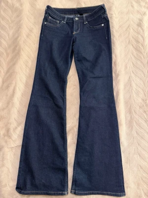 Mörkblå bootcut jeans - Snygga mörkblå bootcut jeans med klassisk femficksdesign och kontrastsömmar. Jeansen har medel/låg midja och bootcut ben, vilket ger en retroinspirerad look. Tillverkade i ett mjukt och stretchigt denimtyg för extra komfort.