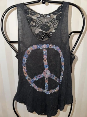 M.a.p.p  linne med spets och peace-märke - Säljer ett svart linne med blommigt peace-märke framtill och hel rygg i genombruten spets. Materialet är tunt och luftigt, perfekt för sommaren. Linnet har en avslappnad passform och cool boho-vibe.Italiensk storlek XL europeisk M.