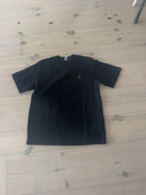 Svart ralph lauren t-shirt med liten röd detalj - Svart t-shirt i bomull med en liten röd detalj på bröstet. Klassisk rund halsringning och korta ärmar. Perfekt för dig som gillar enkel och stilren design.