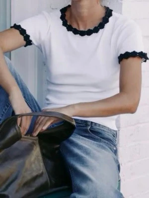 Vit topp med svarta volangdetaljer - Snygg vit topp med svarta volangdetaljer vid halsringning och ärmslut. Kortärmad och figurnära passform, perfekt till jeans eller kjol. Enkel men ändå unik design som sticker ut.