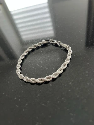 Cordell Armband Silver  - Stilrent armband i silverfärg med flätad design och metalllås. Perfekt för dig som gillar minimalistiska accessoarer med en twist. Armbandet har en klassisk form och passar till många olika outfits.