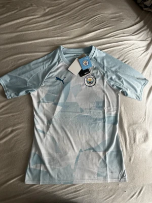 Manchester City matchtröja Puma - ORGINAL OBS!! Riktig pris 799kr Snygg Manchester City matchtröja från Puma i ljusblått och vitt med klubbmärke på bröstet och Puma-logga. Tillverkad i ett lätt och ventilerande funktionsmaterial, perfekt för fotboll eller träning. Kortärmad och med modern passform.