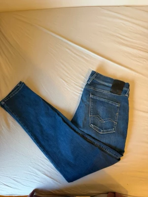 Blå slim fit jeans från Replay - Säljer ett par klassiska blå slim fit jeans från Replay. Jeansen har fem fickor, snygga kontrastsömmar och en svart läderpatch bak i midjan. Tillverkade i slitstark denim med en tidlös tvätt och smal passform.