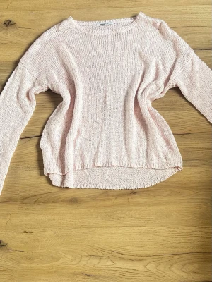 Ljusrosa stickad tröja. Gina - Mysig ljusrosa stickad tröja med rund halsringning och långa ärmar. Tröjan har en avslappnad passform och ribbade kanter vid ärmslut och nederkant. Perfekt för lager på lager under kyligare dagar.