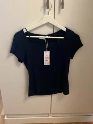 Mörkblå kortärmad topp - Snygg mörkblå topp med korta ärmar och rak, något croppad passform. Tillverkad i mjuk bomullsmix och har en stilren, enkel design med rundad halsringning. Perfekt att matcha med jeans eller kjol.