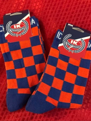 Rutiga IK Oskarshamn strumpor st. 36-39 , 2 st.  - Snygga strumpor från IK Oskarshamn med rutigt mönster i blått och orange. Perfekta för dig som vill visa ditt stöd för laget! Strumporna har klubbens logga och text upptill. Tillverkade i mjukt material för skön känsla.