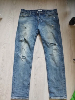 Blå slitna jeans Comfort Fit Mike - Säljer ett par blå jeans med slitningar och hål på benen, modell Comfort Fit Mike. Jeansen har klassisk femficksdesign och raka ben. Perfekta för en avslappnad och trendig look.