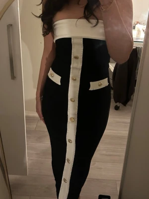 Svart och vit tubklänning med knappar - Säljer en svart tubklänning med vita detaljer och guldknappar framtill. Helt ny och aldrig använt köpt för 499💕storlek S men skulle säga att den är ganska tajt och även kan passa xs