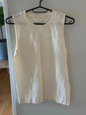 Vit ärmlös linnetopp - Säljer en stilren vit linnetopp med rund halsringning och meshdetaljer upptill. Toppen är ärmlös och har en enkel, clean look som passar perfekt till sommaren. Materialet känns lätt och luftigt, perfekt för varma dagar.