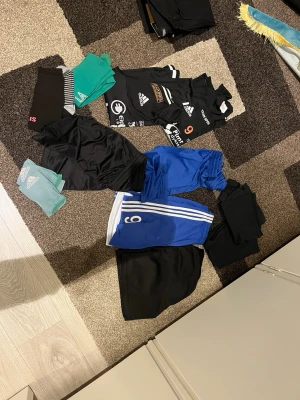 Träningskläder - 4 par shorts (2 svarta 2 blåa) 20kr styck 1 par underställ både övre och under del 20kr 2 långärmade träningströjor med fotbollslaget Fkk på.  15kr styck 3 par fotbollsstrumpor (2 gröna, ett par är klippta) (1 par svarta som det står paris på)  10kr styck  130kr för allt